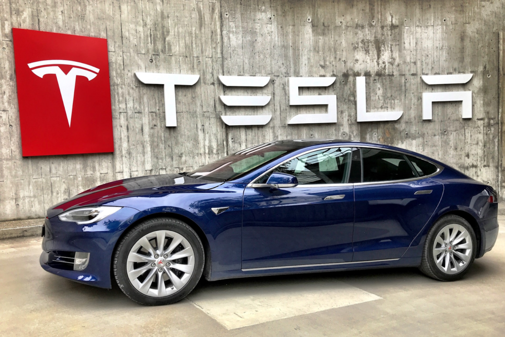 Tesla model parked in front of Tesla logo.
