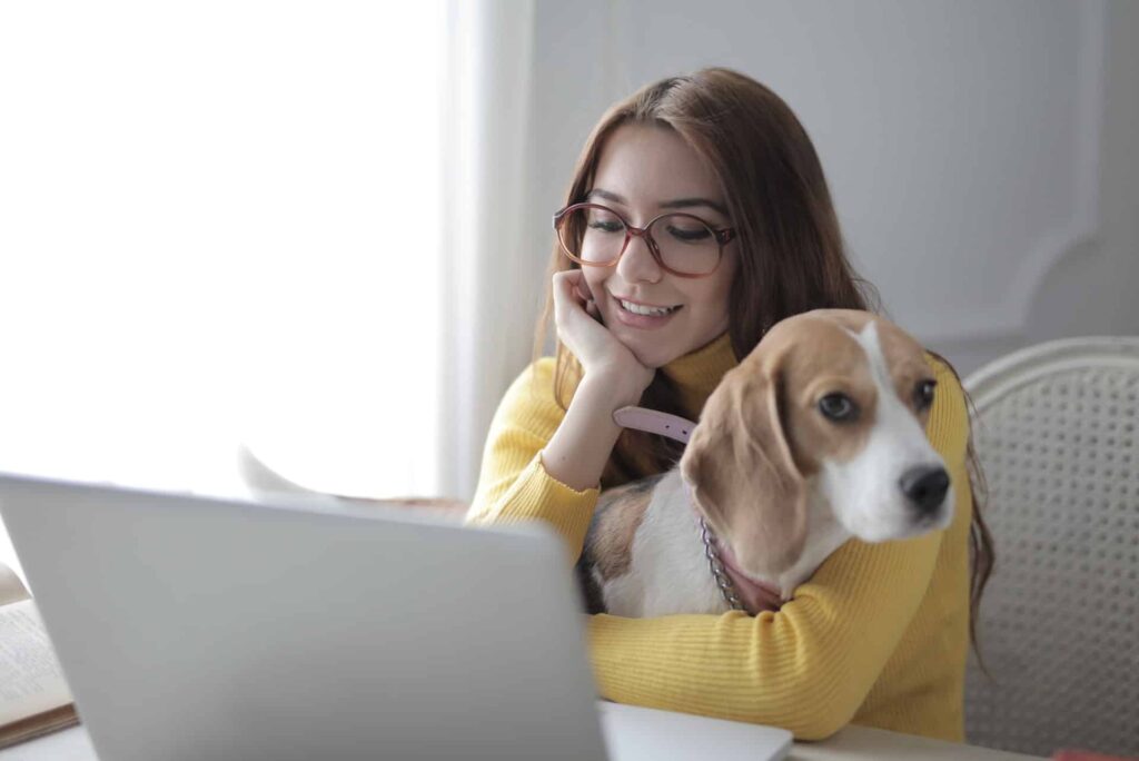 A woman holding her dog while looking at her laptop. 